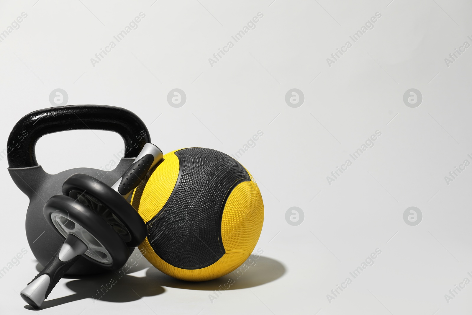Photo of Medicine ball, ab wheel and kettlebell on light grey background, space for text
