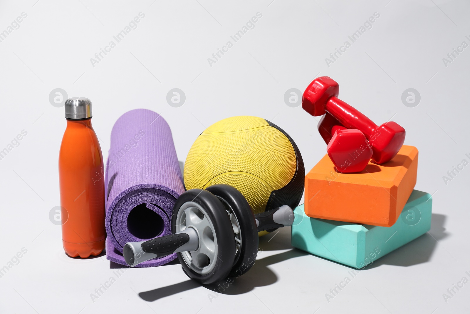 Medicine ball, dumbbells, ab wheel, foam blocks, water bottle and fitness mat on light grey background Photo of Medicine ball, dumbbells, ab wheel, foam blocks, water bottle and fitness mat on light grey background