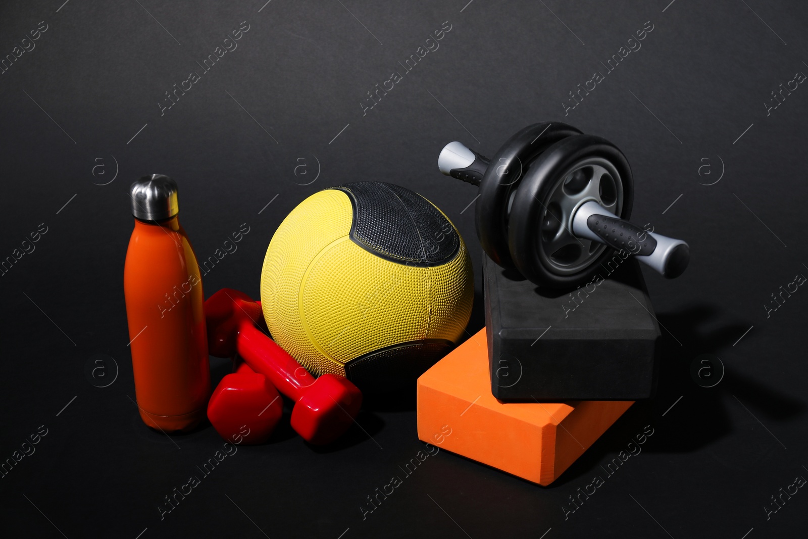 Medicine ball, dumbbells, ab wheel, water bottle and foam blocks on black background Photo of Medicine ball, dumbbells, ab wheel, water bottle and foam blocks on black background
