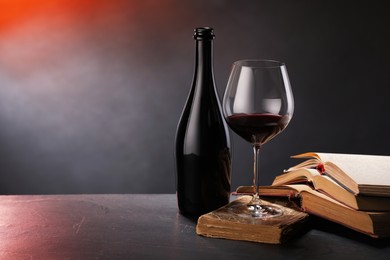 Photo of Tasty wine and books on dark textured table in color light, closeup. Space for text