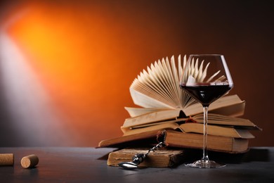 Photo of Red wine in glass and books on dark textured table in color lights. Space for text