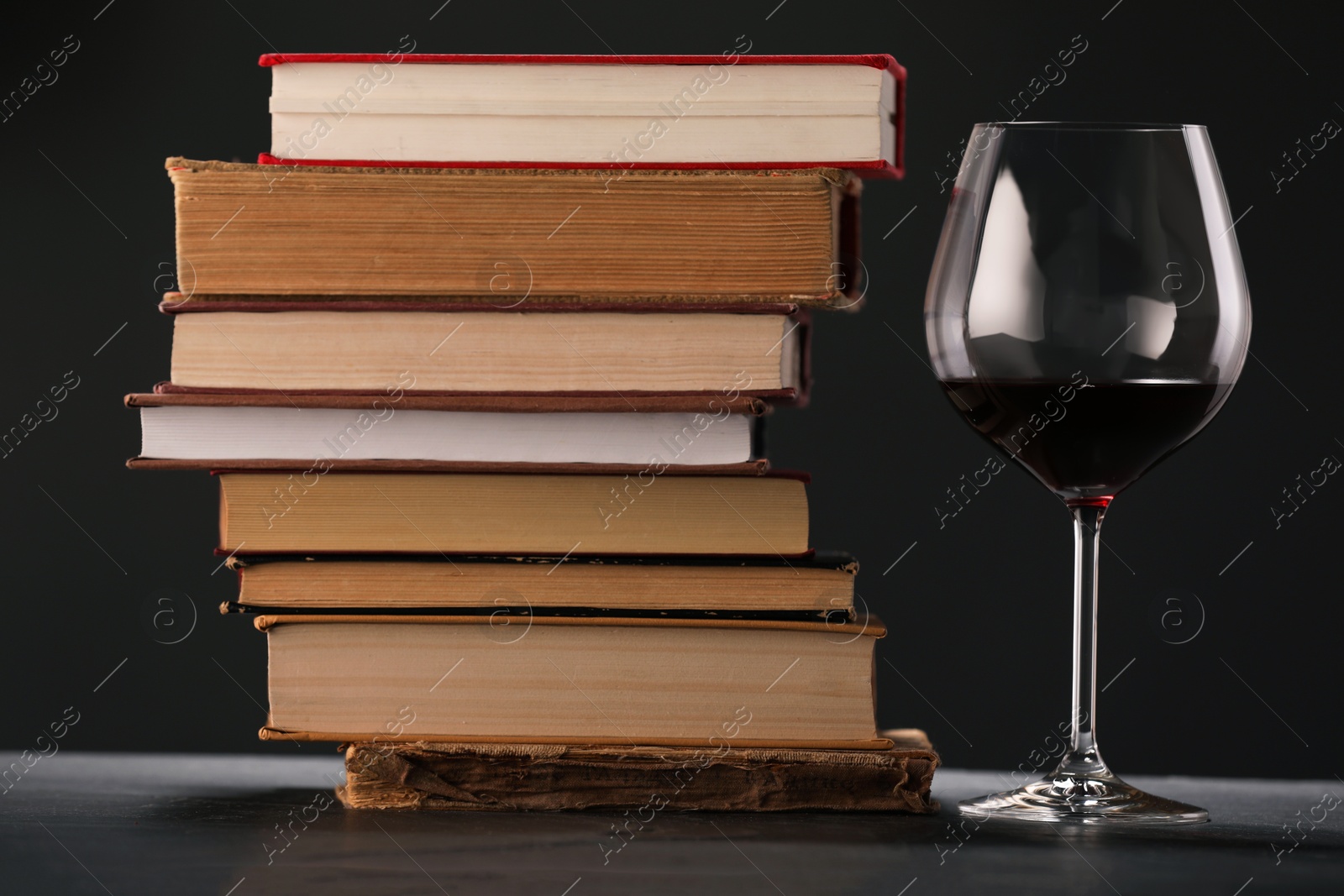 Red wine in glass and stack of books on grey textured table against black background, closeup Photo of Red wine in glass and stack of books on grey textured table against black background, closeup