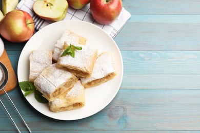 Photo of Pieces of tasty apple strudel with powdered sugar, mint and fruits on light blue wooden table, flat lay. Space for text