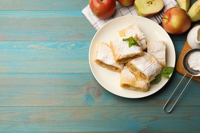 Photo of Pieces of tasty apple strudel with powdered sugar, mint and fruits on light blue wooden table, flat lay. Space for text