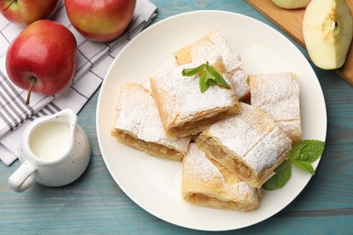 Photo of Pieces of tasty apple strudel with powdered sugar, mint and fruits on light blue wooden table, flat lay