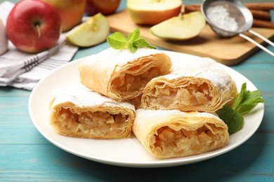 Photo of Pieces of tasty apple strudel with powdered sugar and mint on light blue wooden table, closeup