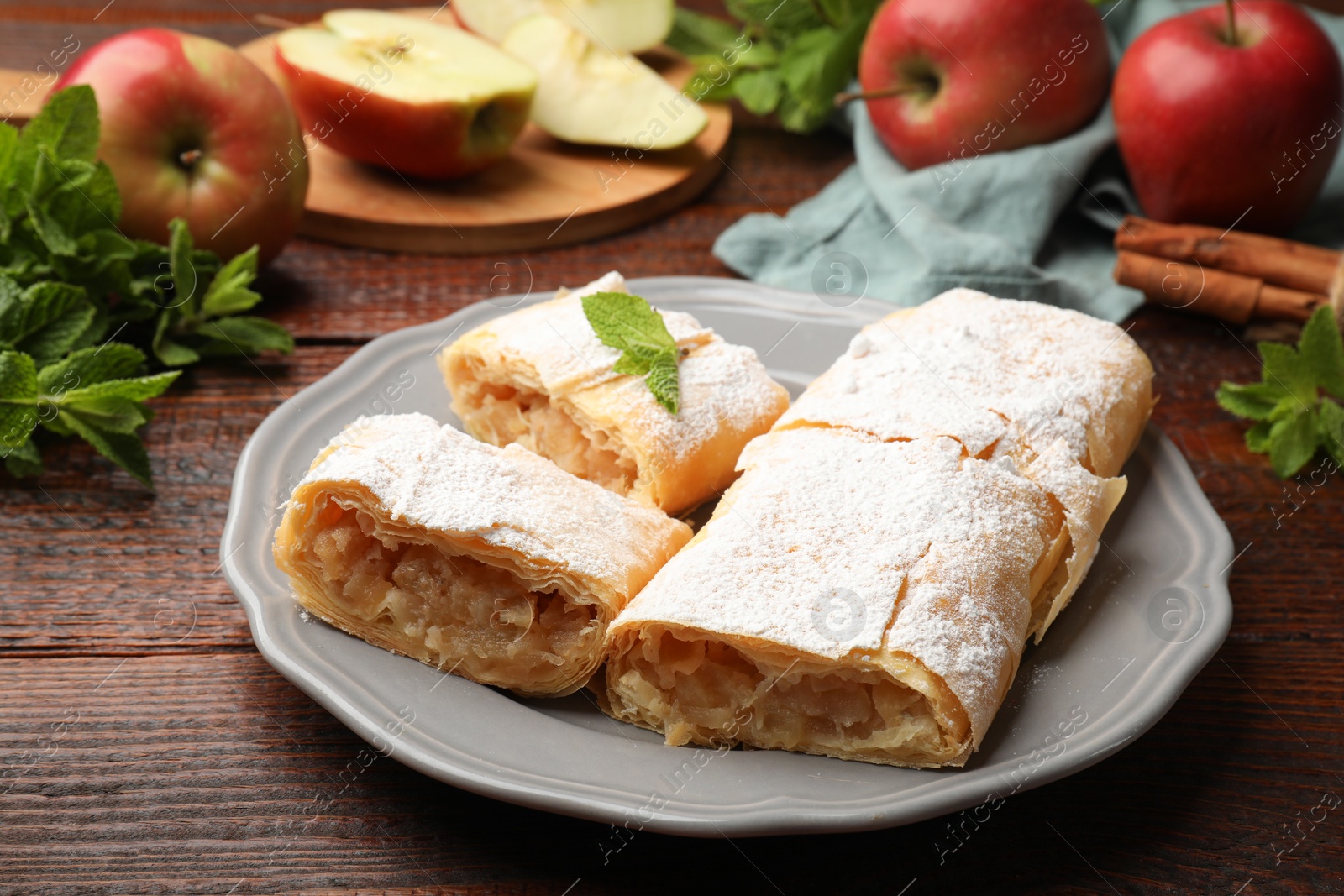 Pieces of tasty apple strudel with powdered sugar, mint and fruits on wooden table, closeup Photo of Pieces of tasty apple strudel with powdered sugar, mint and fruits on wooden table, closeup