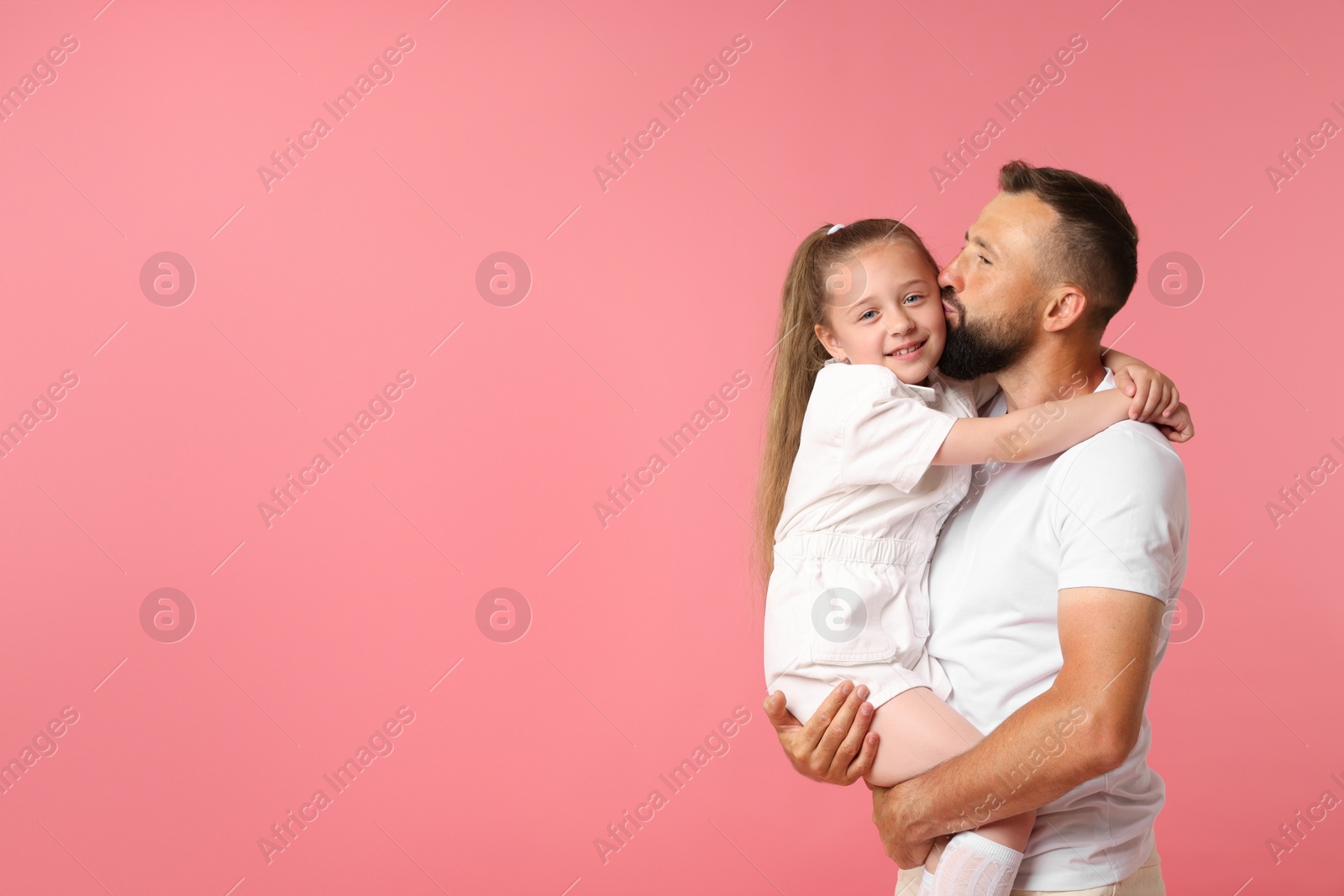 Family. Father kissing his happy daughter on pink background. Space for text Photo of Family. Father kissing his happy daughter on pink background. Space for text
