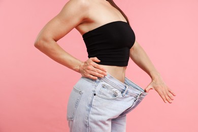 Photo of Fit woman wearing old jeans after weight loss on pink background, closeup