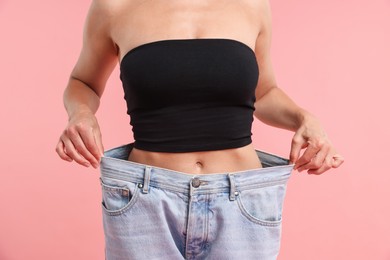 Photo of Fit woman wearing old jeans after weight loss on pink background, closeup