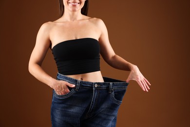 Photo of Fit woman wearing old jeans after weight loss on brown background, closeup