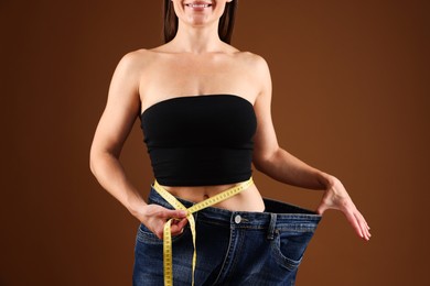 Photo of Fit woman with measuring tape wearing old jeans after weight loss on brown background, closeup