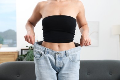 Photo of Fit woman wearing old jeans after weight loss at home, closeup