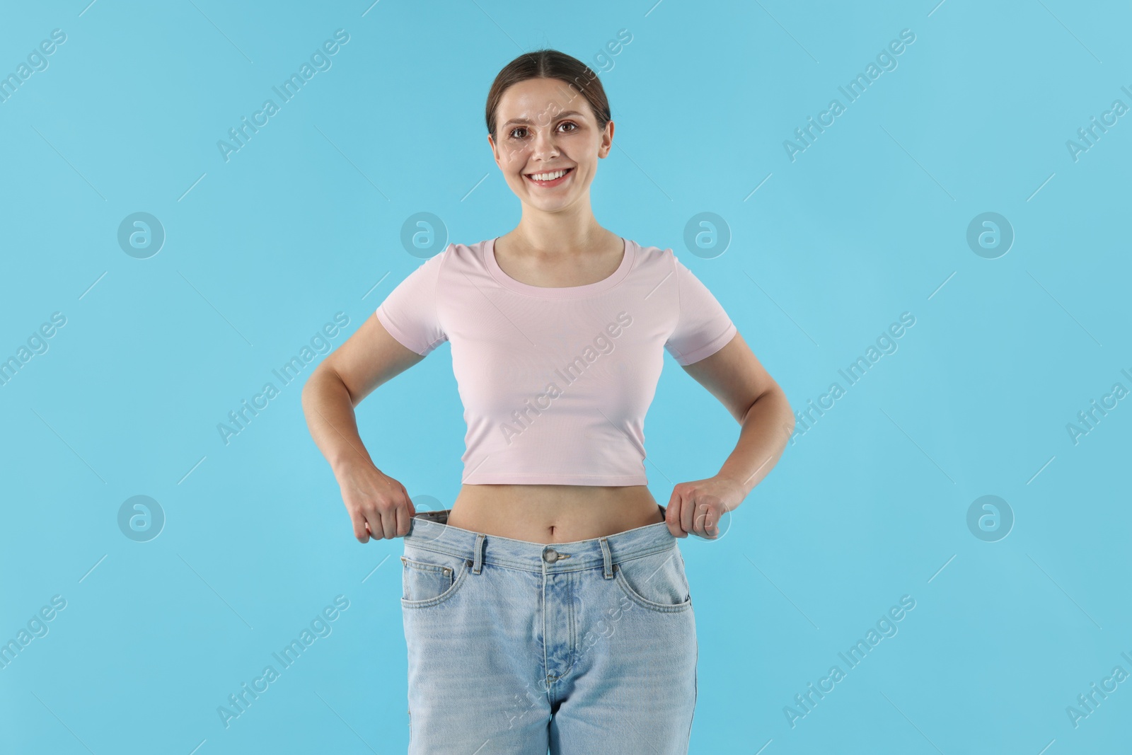 Beautiful woman wearing old jeans after weight loss on light blue background Photo of Beautiful woman wearing old jeans after weight loss on light blue background