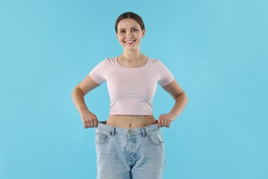 Photo of Beautiful woman wearing old jeans after weight loss on light blue background