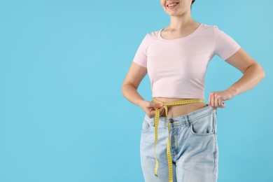 Photo of Woman with measuring tape wearing old jeans after weight loss on light blue background, closeup. Space for text