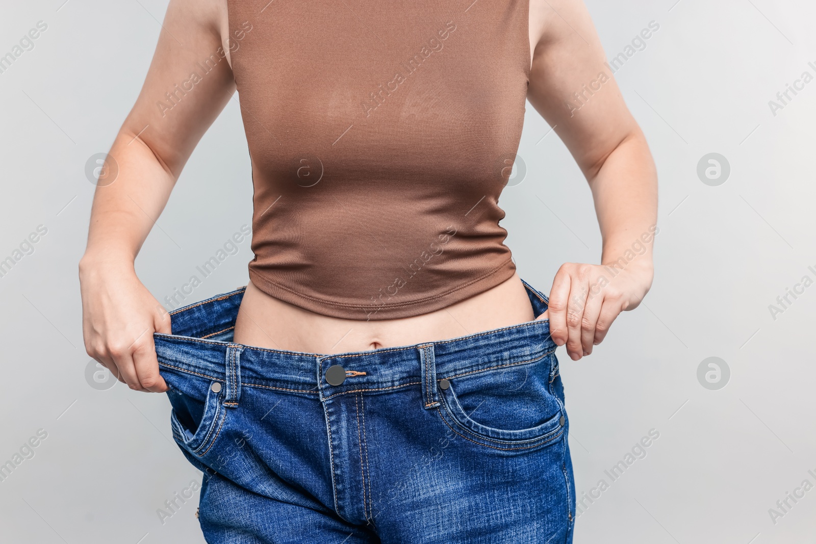 Woman wearing old jeans after weight loss on light grey background, closeup Photo of Woman wearing old jeans after weight loss on light grey background, closeup
