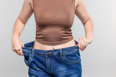 Photo of Woman wearing old jeans after weight loss on light grey background, closeup