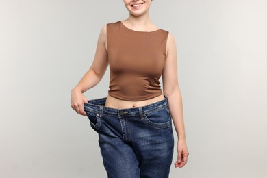 Photo of Woman wearing old jeans after weight loss on light grey background, closeup