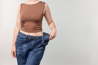 Photo of Woman wearing old jeans after weight loss on light grey background, closeup. Space for text