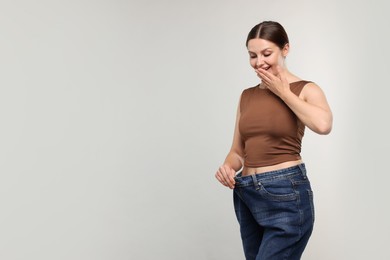 Photo of Beautiful woman wearing old jeans after weight loss on light grey background, space for text