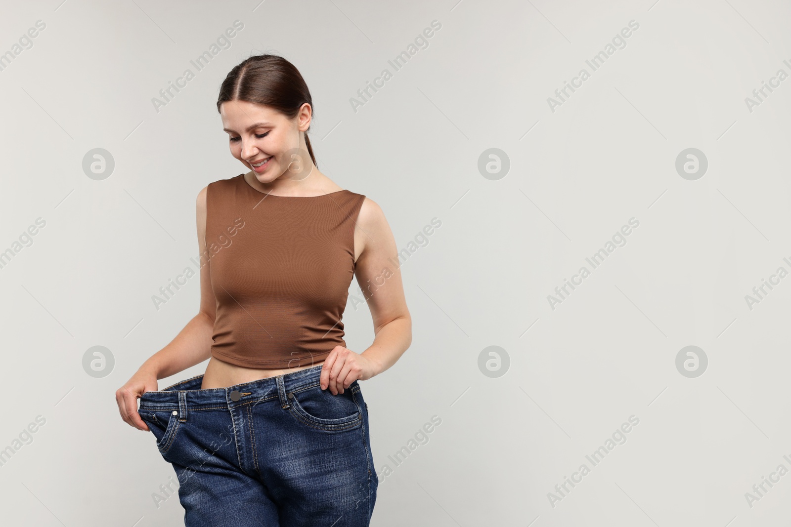 Beautiful woman wearing old jeans after weight loss on light grey background, space for text Photo of Beautiful woman wearing old jeans after weight loss on light grey background, space for text