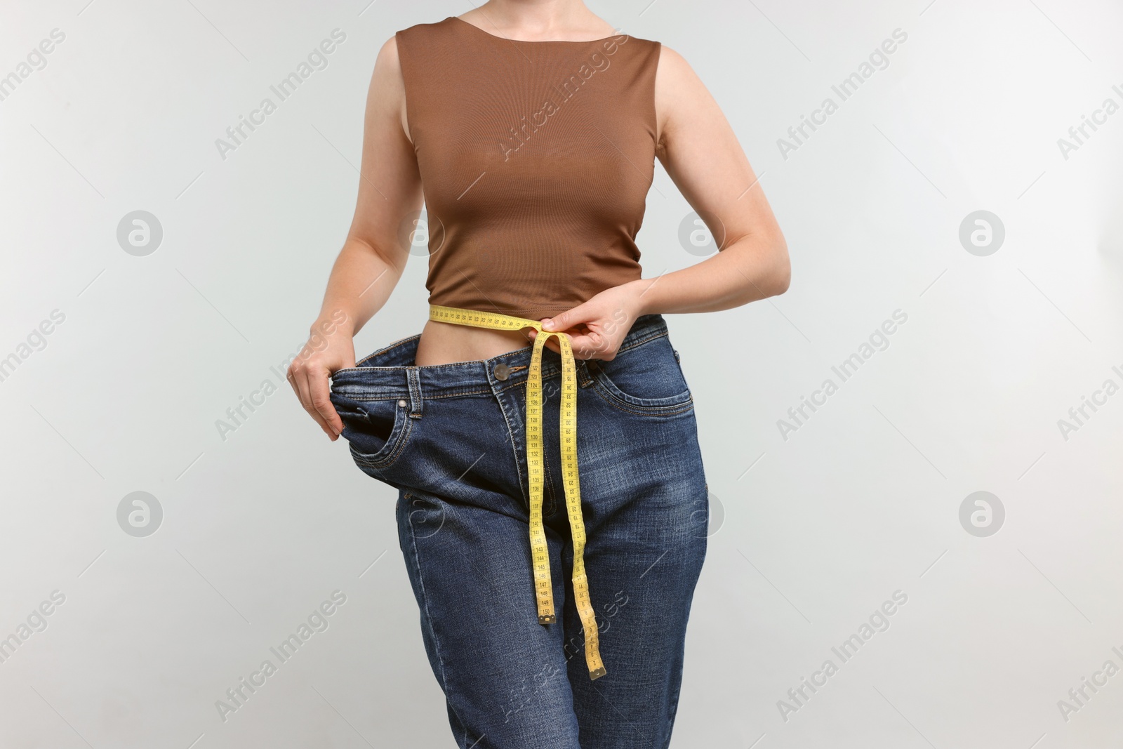 Woman with measuring tape wearing old jeans after weight loss on light grey background, closeup Photo of Woman with measuring tape wearing old jeans after weight loss on light grey background, closeup