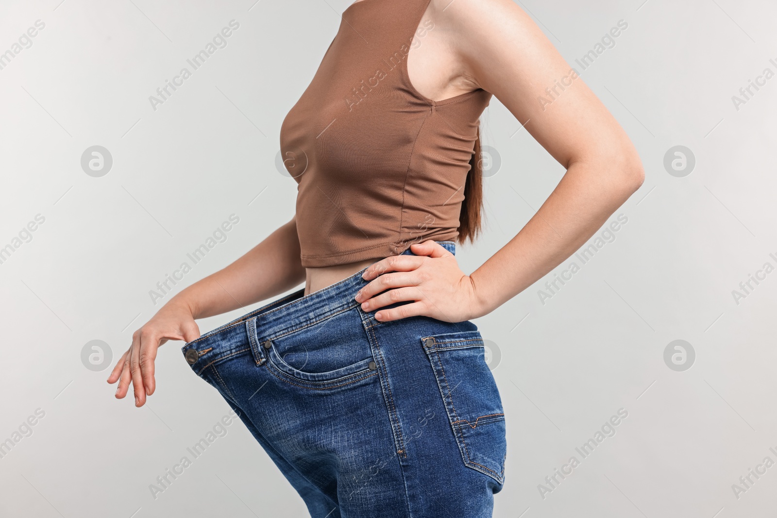 Woman wearing old jeans after weight loss on light grey background, closeup Photo of Woman wearing old jeans after weight loss on light grey background, closeup