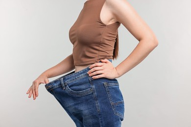 Photo of Woman wearing old jeans after weight loss on light grey background, closeup