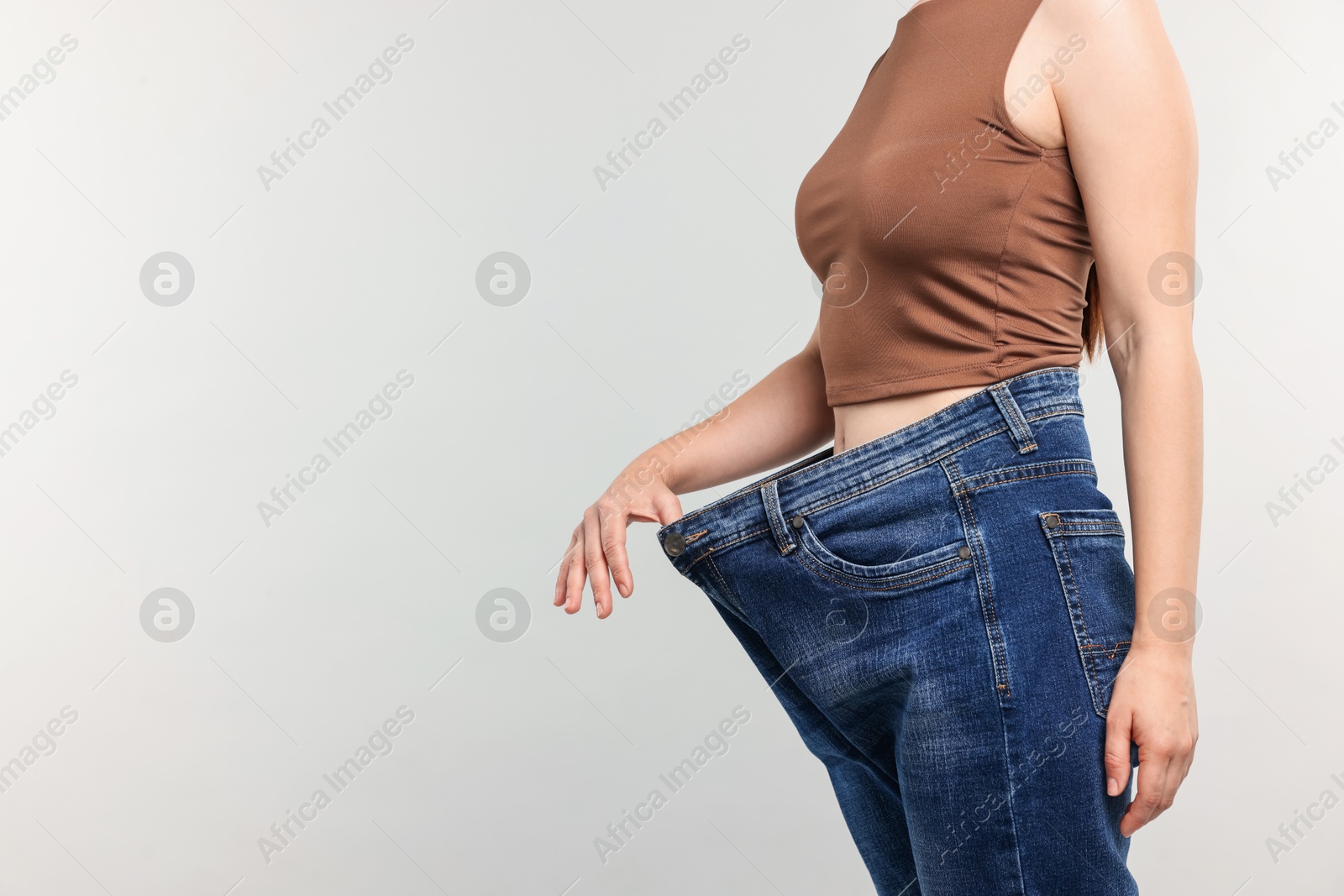 Woman wearing old jeans after weight loss on light grey background, closeup. Space for text Photo of Woman wearing old jeans after weight loss on light grey background, closeup. Space for text