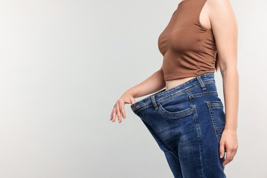 Photo of Woman wearing old jeans after weight loss on light grey background, closeup. Space for text