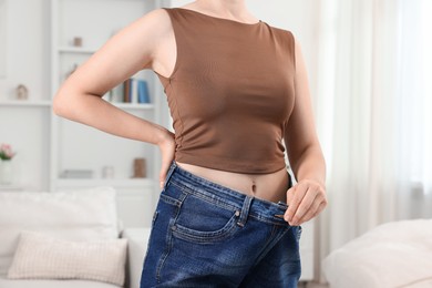 Photo of Woman wearing old jeans after weight loss indoors, closeup