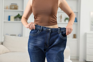 Photo of Woman wearing old jeans after weight loss indoors, closeup
