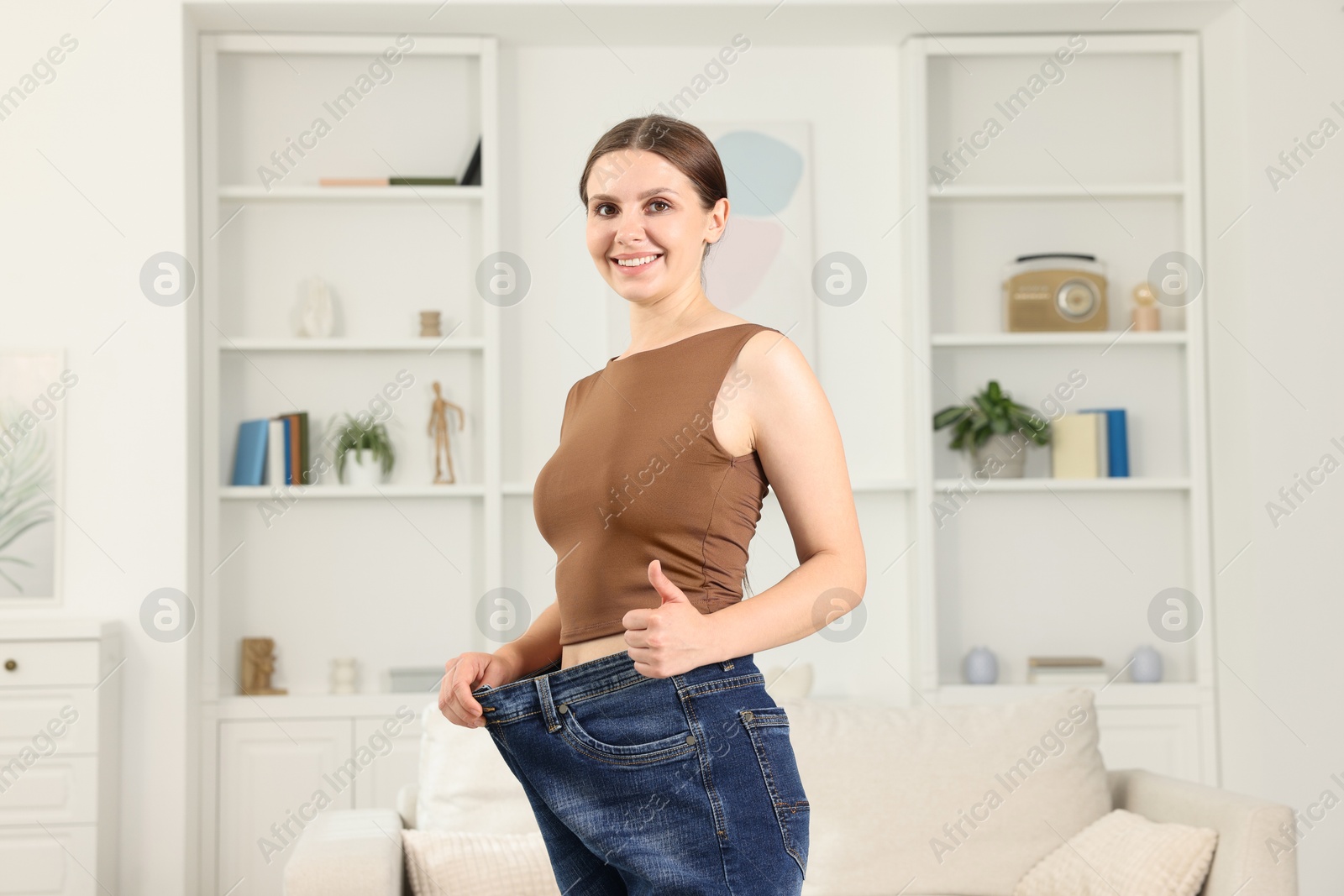 Beautiful woman wearing old jeans after weight loss and showing thumbs up indoors Photo of Beautiful woman wearing old jeans after weight loss and showing thumbs up indoors