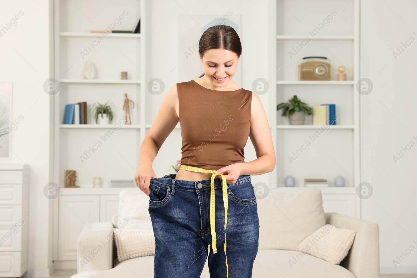 Beautiful woman with measuring tape wearing old jeans after weight loss indoors Photo of Beautiful woman with measuring tape wearing old jeans after weight loss indoors