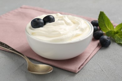 Photo of Delicious yogurt in bowl, blueberries, mint and spoon on grey table, closeup