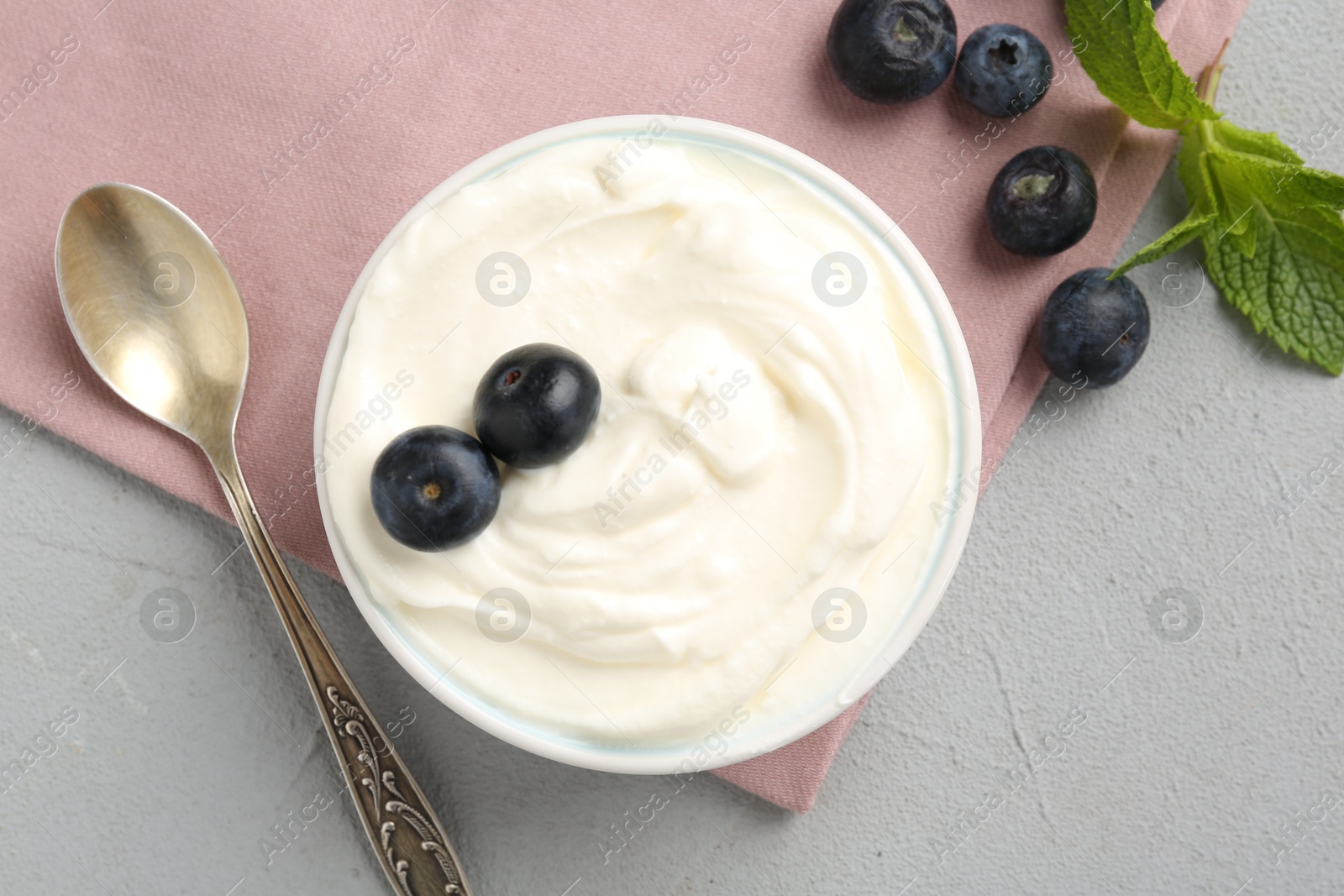 Photo of Delicious yogurt in bowl, blueberries, mint and spoon on grey table, flat lay
