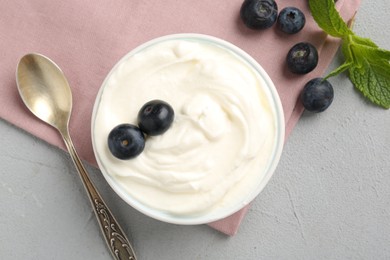 Photo of Delicious yogurt in bowl, blueberries, mint and spoon on grey table, flat lay
