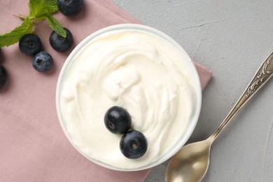 Photo of Delicious yogurt in bowl, blueberries, mint and spoon on grey table, flat lay