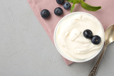 Photo of Delicious yogurt in bowl, blueberries, mint and spoon on grey table, flat lay. Space for text