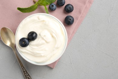 Photo of Delicious yogurt in bowl, blueberries, mint and spoon on grey table, flat lay. Space for text