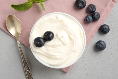 Photo of Delicious yogurt in bowl, blueberries, mint and spoon on grey table, flat lay