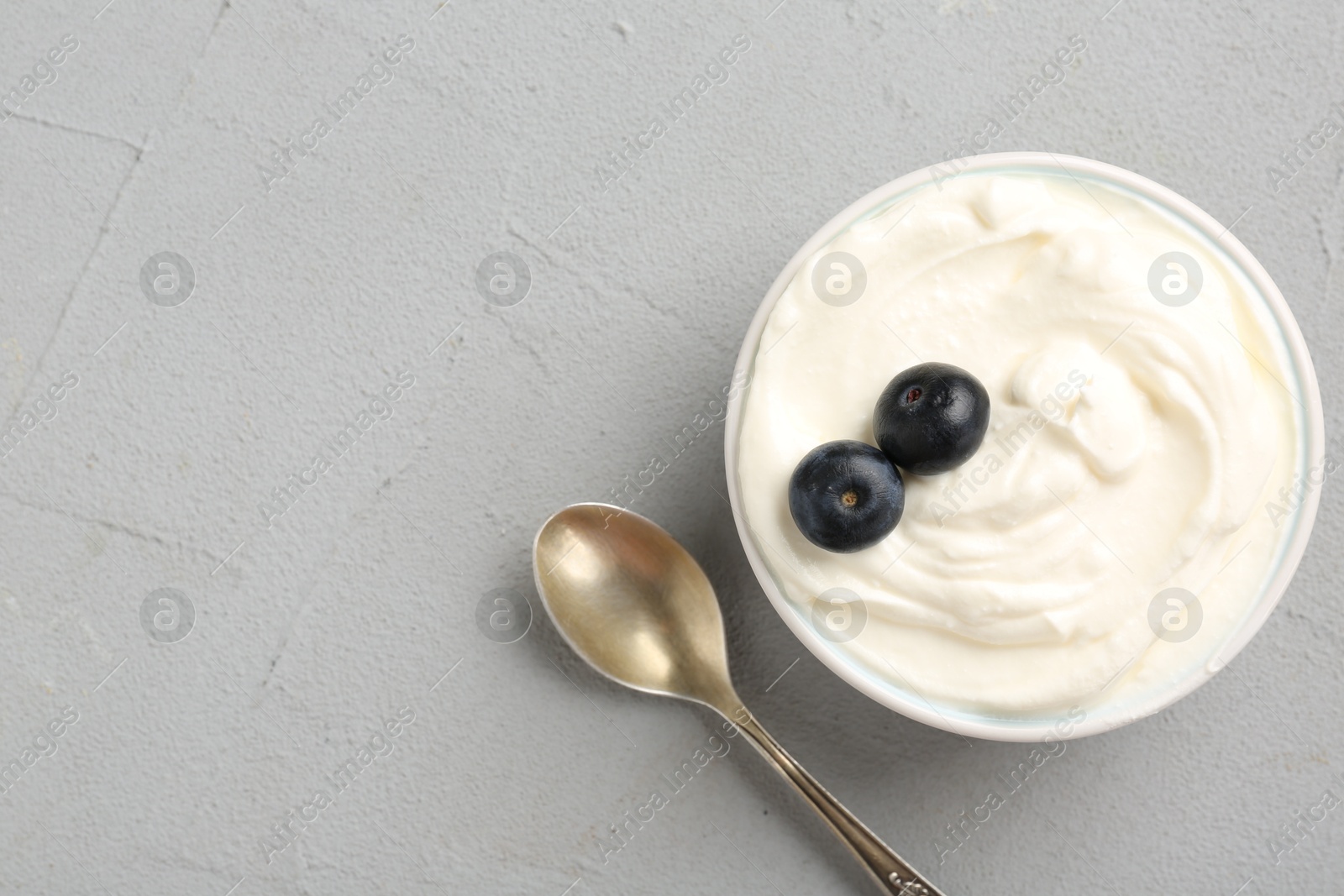 Delicious yogurt in bowl, blueberries and spoon on grey table, flat lay. Space for text Photo of Delicious yogurt in bowl, blueberries and spoon on grey table, flat lay. Space for text