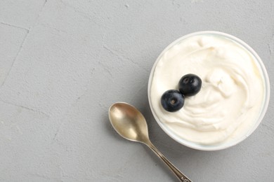 Photo of Delicious yogurt in bowl, blueberries and spoon on grey table, flat lay. Space for text