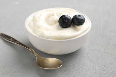 Photo of Delicious yogurt in bowl, blueberries and spoon on grey table, closeup