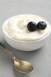 Photo of Delicious yogurt in bowl, blueberries and spoon on grey table, closeup