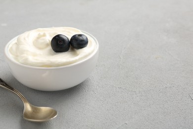 Photo of Delicious yogurt in bowl, blueberries and spoon on grey table, closeup. Space for text