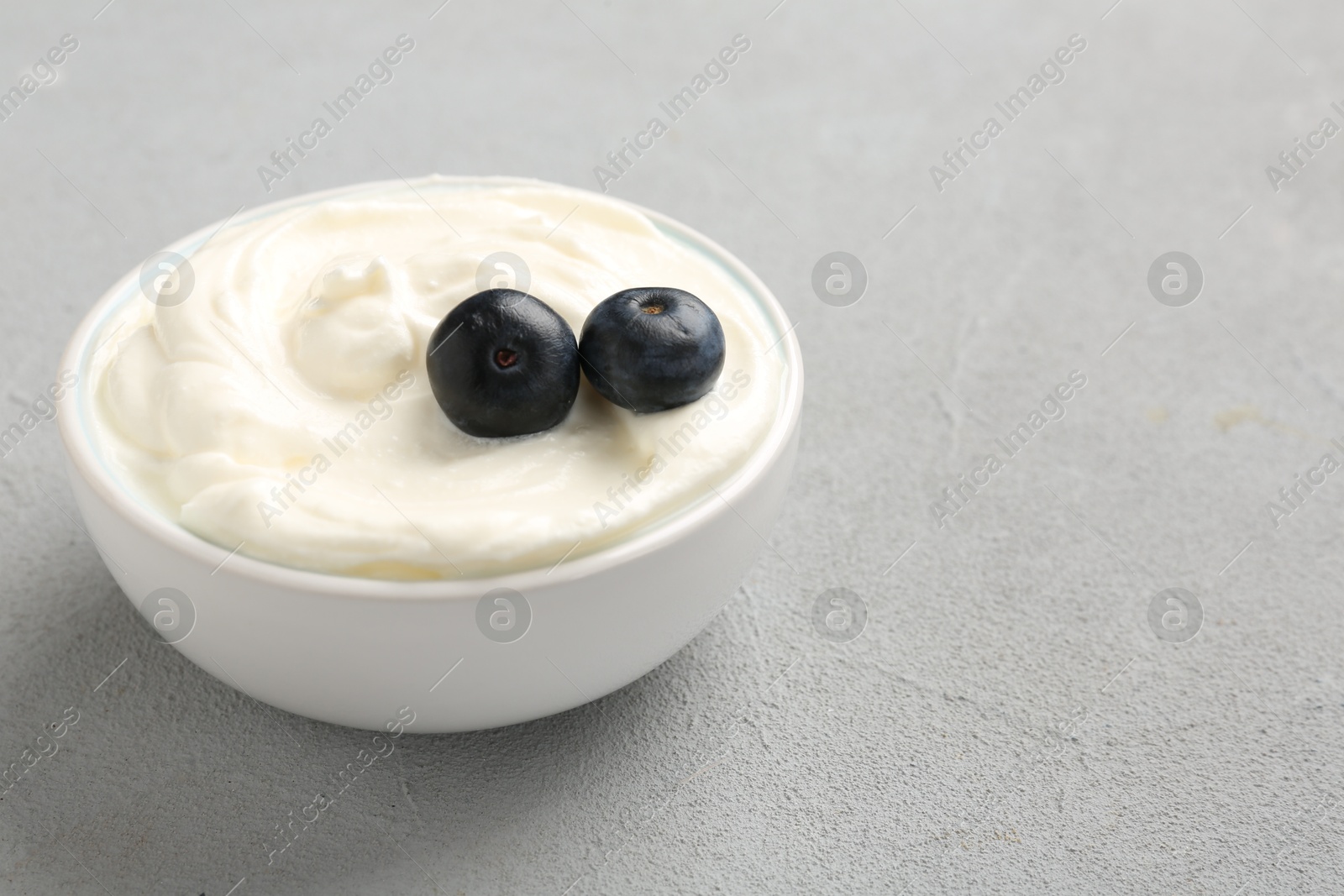 Photo of Delicious yogurt with blueberries in bowl on grey table, closeup. Space for text