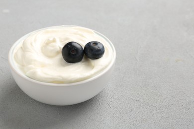 Photo of Delicious yogurt with blueberries in bowl on grey table, closeup. Space for text