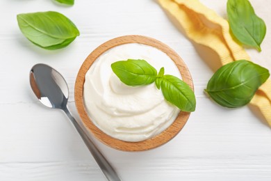 Photo of Delicious yogurt in bowl, basil and spoon on white wooden table, flat lay